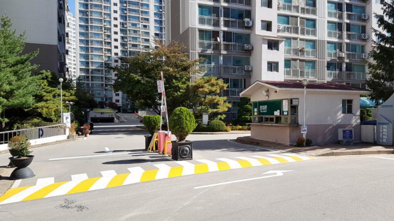 우측에는 경비실이 위치해 있으며, 차량 출입 차단기가 설치되어 있어 외부차량 출입이 제한되는 단지 정문이에요